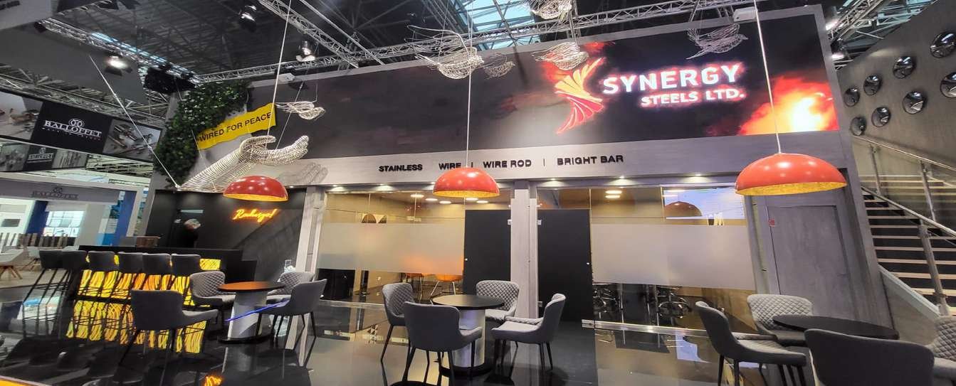 Synergy Steels hospitality stand with black-and-red fascia, meeting tables and enclosed rooms at SSW in Maastricht